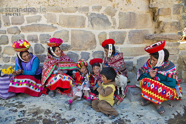 Frauen und Kinder in traditioneller Kleidung der Quechua-Indianer sitzen am Boden vor einer Mauer  Ollantaytambo  Urubambatal  Peru