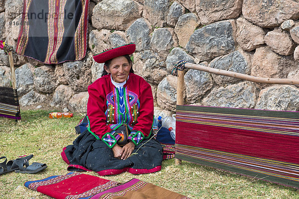 Eine ältere Frau mit Hut  Quechua-Indianer mit traditioneller Kleidung hockt am Boden vor einem Spannrahmen für den Webstuhl  Cinchero  Urubambatal  Peru