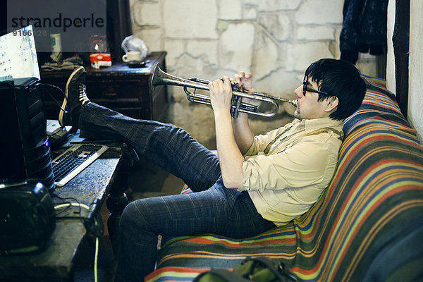 Mari man playing trumpet on sofa