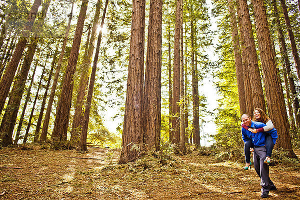 Hispanic man carrying girlfriend piggy back in forest