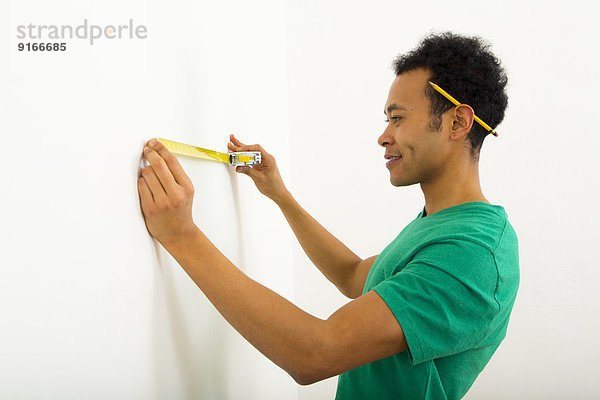 Mixed race man measuring wall