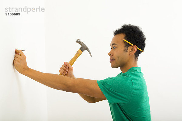 Mixed race man hammering nail into wall