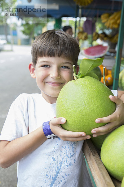 Caucasian boy holding large fruit at market