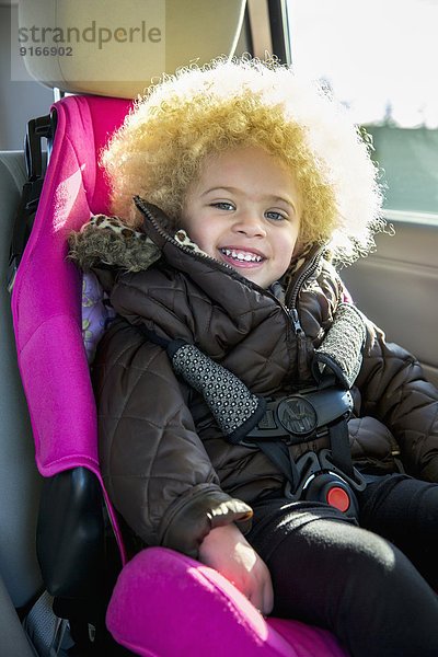 Mixed race girl smiling in back seat of car