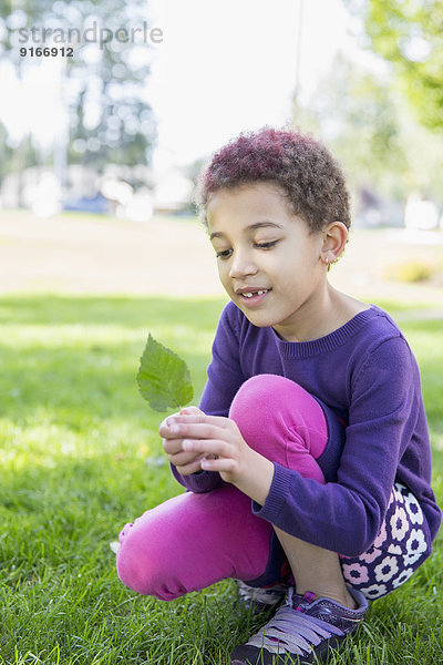 Mixed race girl examining leaf outdoors