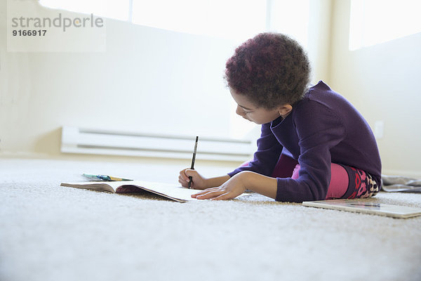 Mixed race girl drawing on bedroom floor