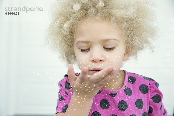 Mixed race girl blowing sparkles from hand