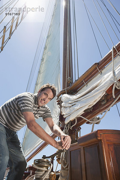 Caucasian man hoisting sail on sailboat