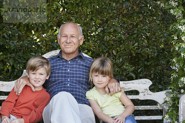 Grandfather sitting with grandchildren on garden bench