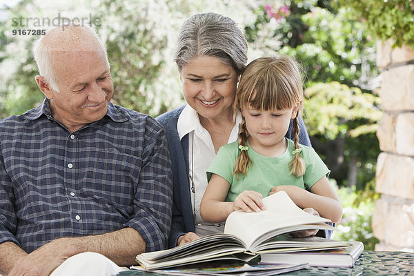 Grandparents and granddaughter reading outdoors