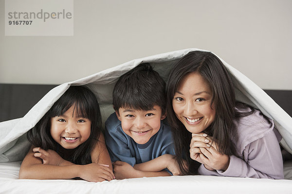 Mother and children laying under bed covers