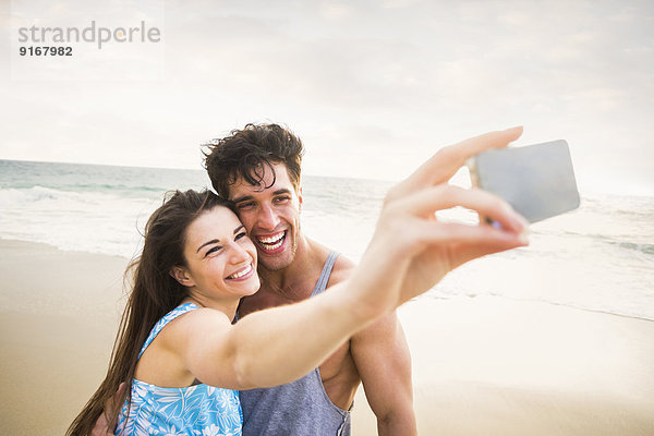 Caucasian couple taking pictures on beach