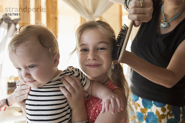 Caucasian girl holding brother as mother brushes her hair