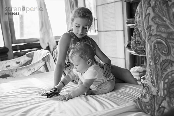 Caucasian girl and baby boy playing on bed