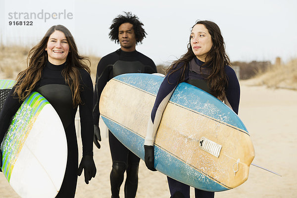 Surfers carrying boards on beach