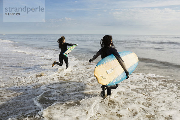 Surfers carrying boards in waves