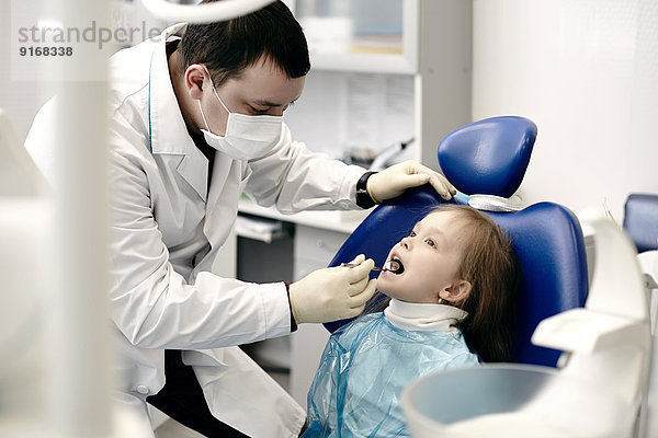 Caucasian dentist examining girl's teeth