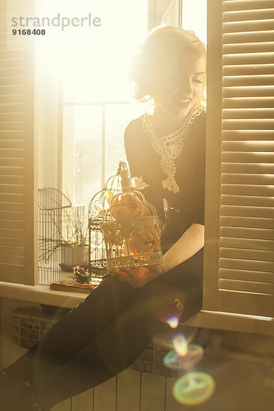 Caucasian woman holding birdcage in window