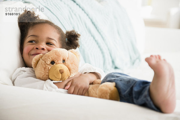 Black girl hugging teddy bear on sofa