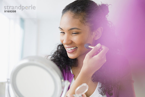 Mixed race woman applying makeup in mirror