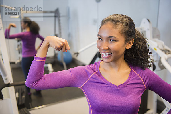 Mixed race woman flexing muscles in gym