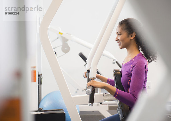 Mixed race woman using exercise machine in gym