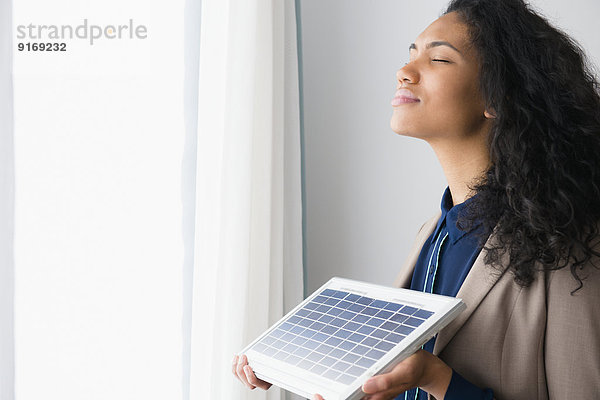 Mixed race woman holding solar panel by window