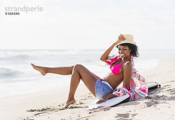 African American woman sitting on surfboard on beach