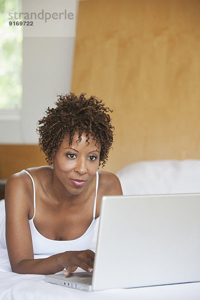 African American woman using laptop on bed