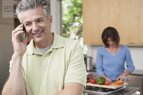 Hispanic man talking on phone in kitchen