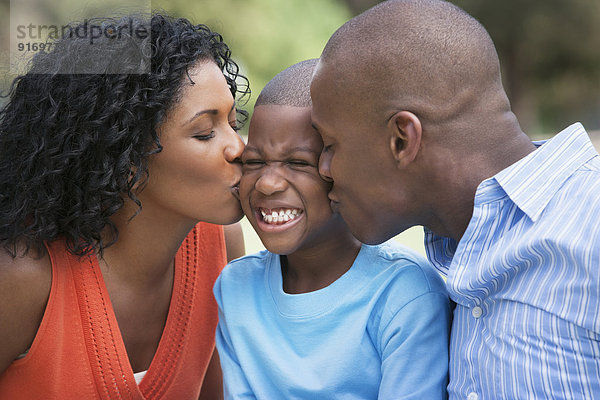 African American parents kissing son's cheeks