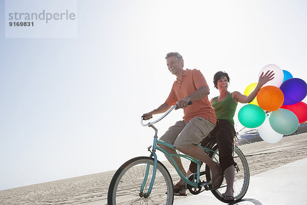 Caucasian couple riding bicycle by beach