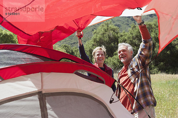 Senior Caucasian couple pitching tent in field