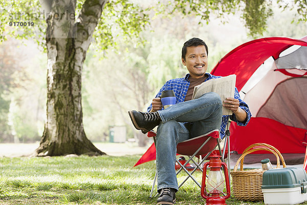 Asian man relaxing in lawn chair at campsite