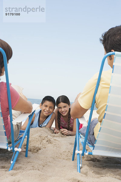 Parents watching children from lawn chairs on beach