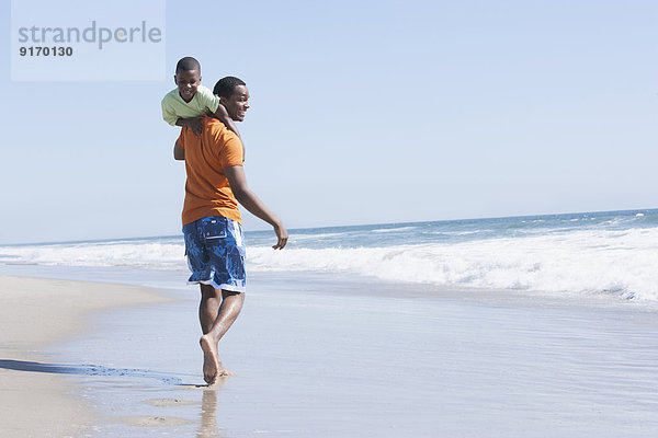 Father carrying son in waves on beach