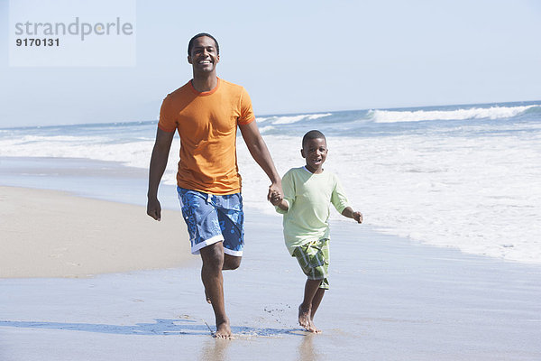 Father and son walking in waves on beach