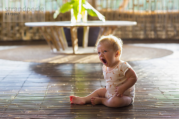 Caucasian baby yawning on floor