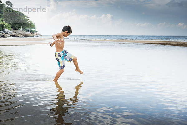 Mixed race boy playing in water on beach