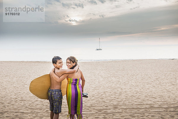 Mixed race children carrying surfboard to ocean