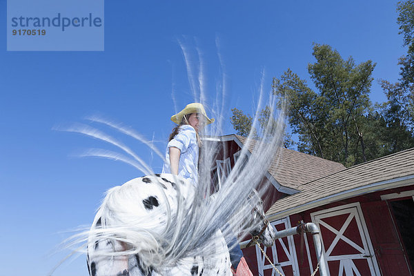 Mixed race girl riding horse on ranch