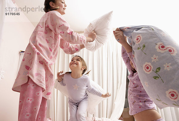 Mixed race girls having pillow fight on bed