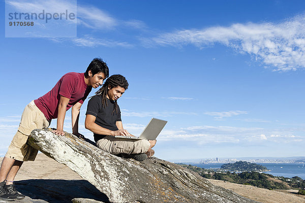 Men using laptop on rocky hilltop