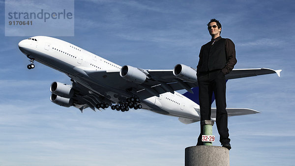 Deutschland  Mittlerer Erwachsener Mann mit Flugzeug im Hintergrund auf Säule stehend