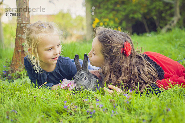 Zwei kleine Mädchen mit Kaninchen auf der Wiese liegend