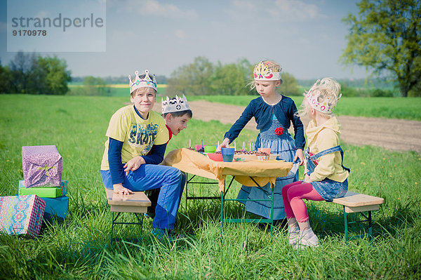 Vier Kinder mit Papierkronen zum Geburtstag auf einer Wiese