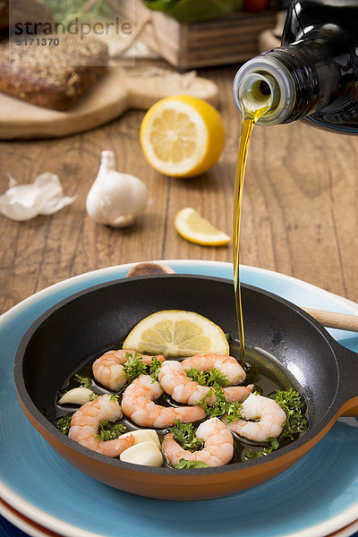 Olive oil is being poured into frying pan with shrimps