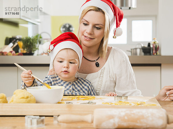 Mutter und Tochter mit Weihnachtsmützen beim Backen in der Küche