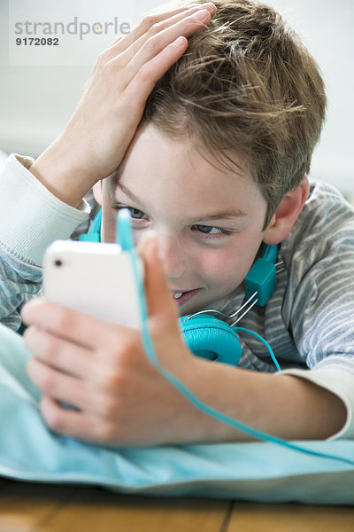 Portrait des Jungen mit Smartphone und Kopfhörer auf Sitzsack liegend