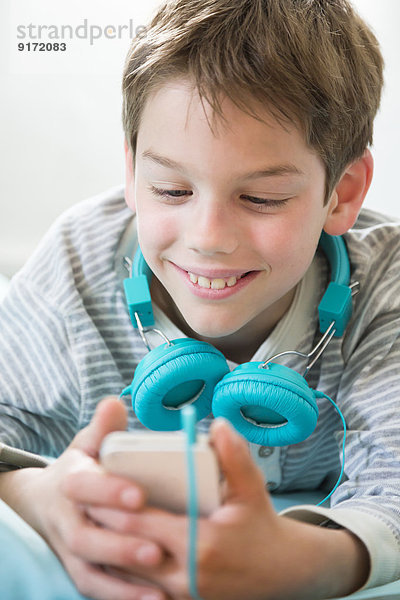 Portrait des lächelnden Jungen mit Smartphone und Kopfhörer auf Sitzsack liegend